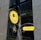 A decorative sign for a cafebar called 'GINZA 328' with a modern design is displayed against a backdrop of a large, reflective building with stone and glass elements. The sign features a bright yellow circular and rectangular design with artistic metalwork, depicting a steaming mug that suggests a welcoming environment.