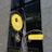 A decorative sign for a cafebar called 'GINZA 328' with a modern design is displayed against a backdrop of a large, reflective building with stone and glass elements. The sign features a bright yellow circular and rectangular design with artistic metalwork, depicting a steaming mug that suggests a welcoming environment.